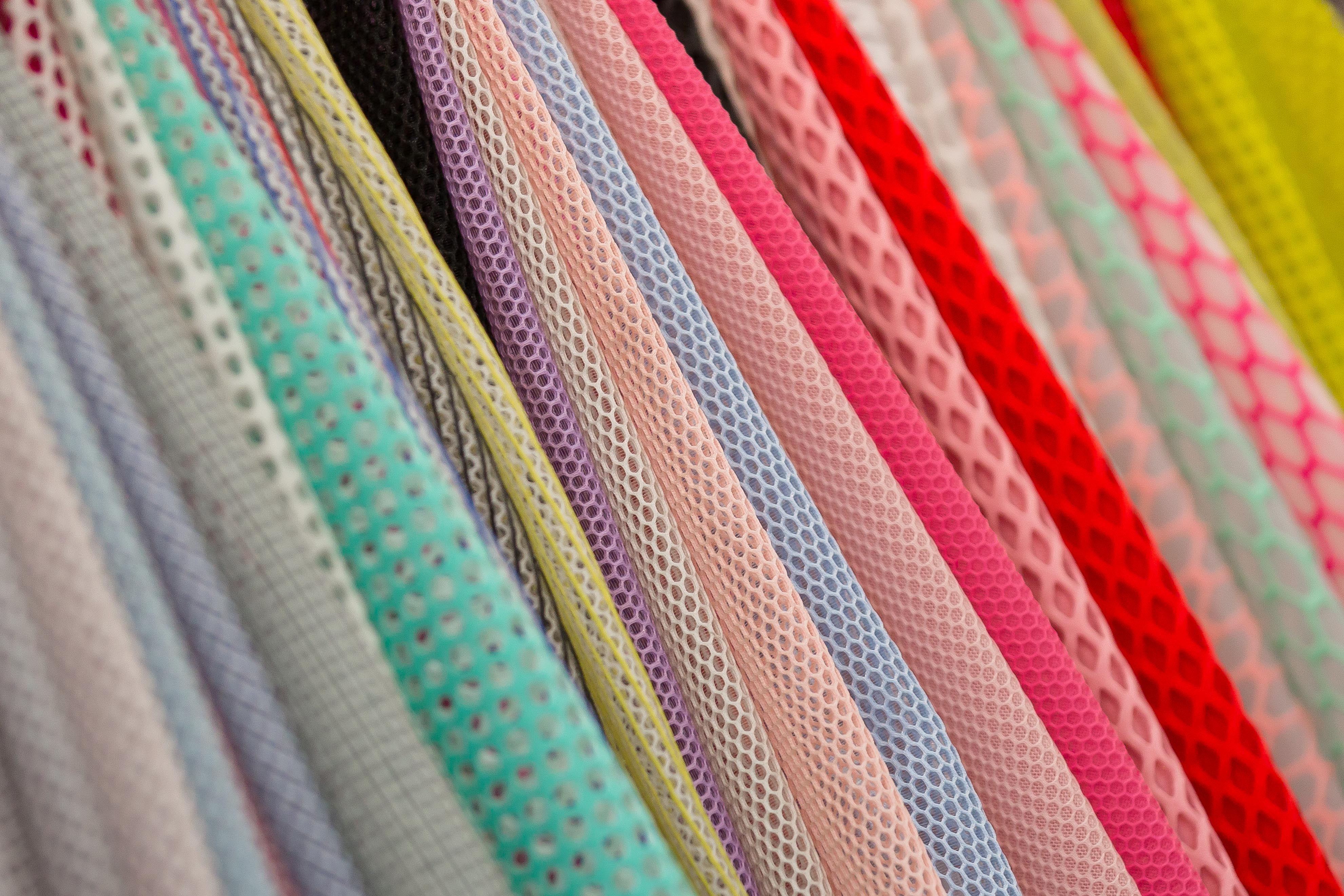 Textiles & Textile Technologies Colorful mesh fabric rolls in various colors, including pink, yellow, and green, displayed at a trade show