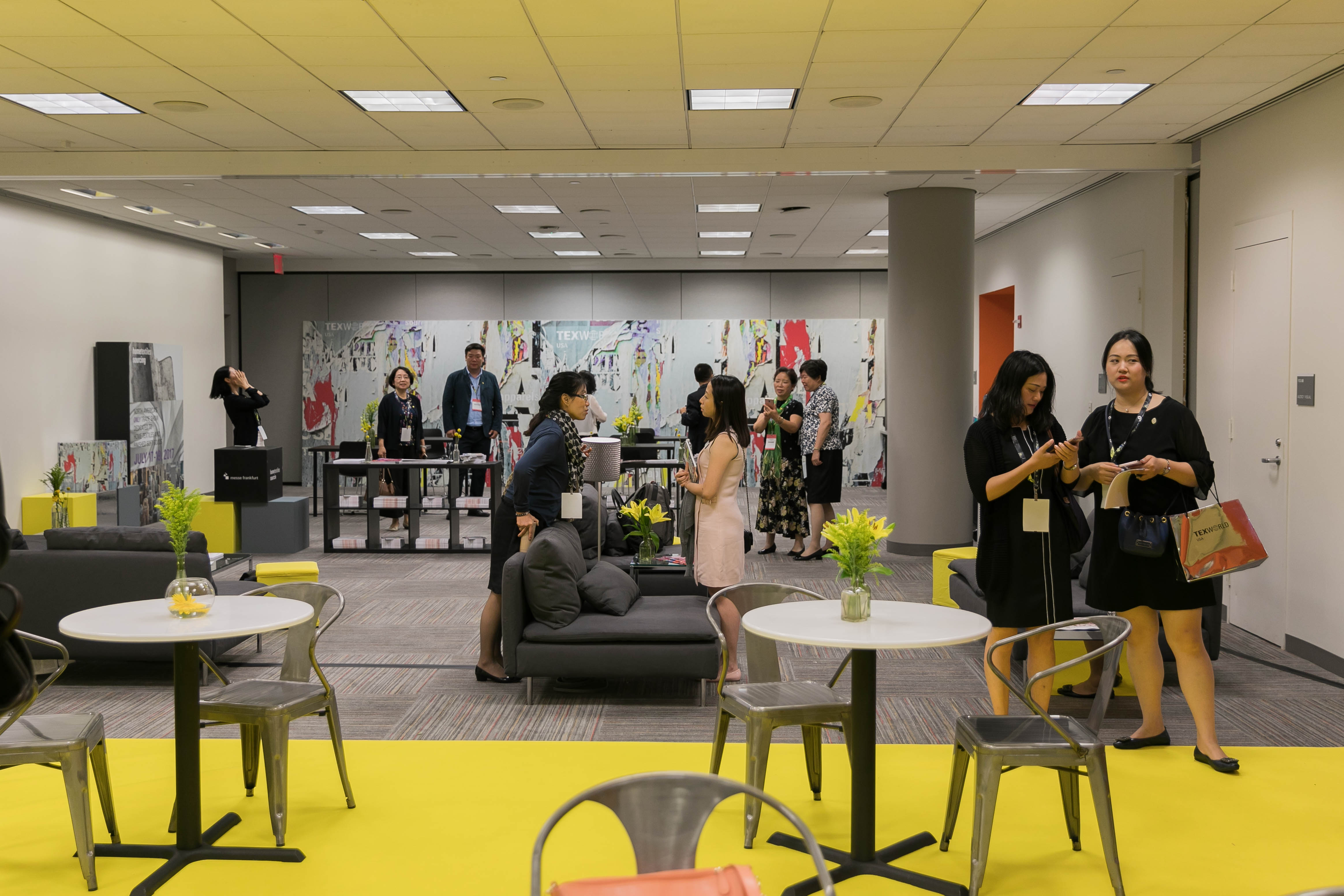 Networking lounge at a trade show, featuring seating areas, yellow flooring, and attendees conversing