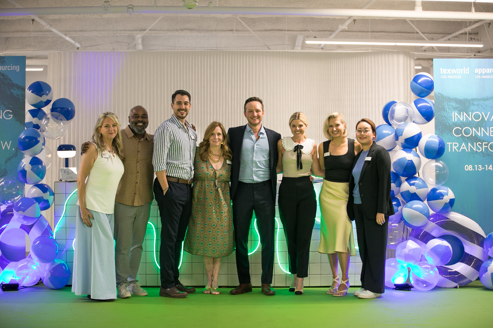 Group photo of event organizers and speakers at Texworld Los Angeles, standing in front of decorative balloons and banners promoting the trade show